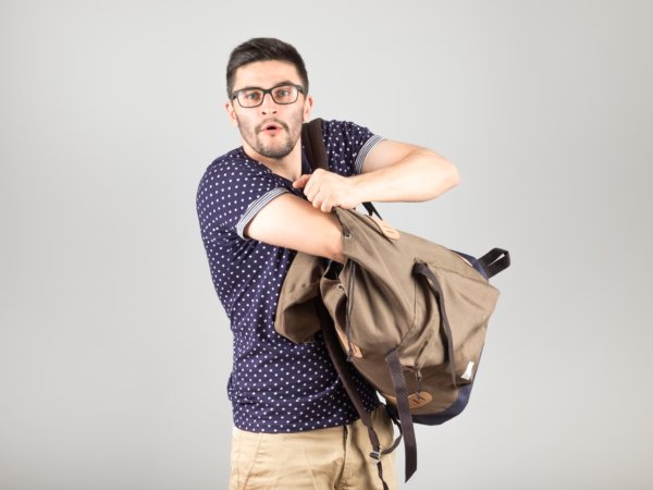 Man standing and getting something out of his backpack isolated on gray