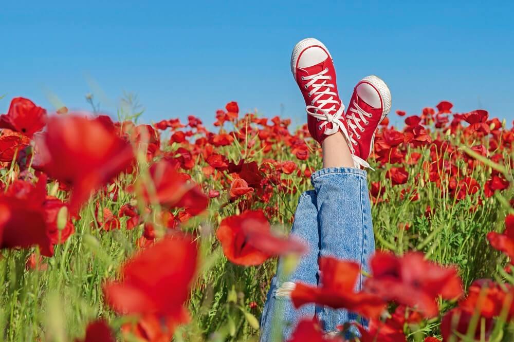 Symbolbild: Der Loop ermöglicht neue Freiheiten im Alltag.  Er schenkt mehr Zeit und energie: Girls legs in red sneakers in a poppy field. Joy and fun concept.
