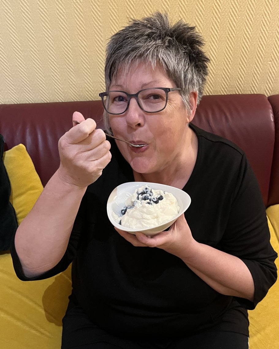 Auf dem Foto ist Susanne zu sehen wie sie einen Nachtisch mit Joghurt und Heidelbeeren isst.